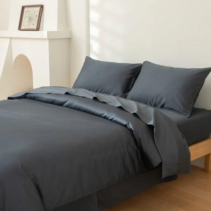 A neatly made bed with dark gray bedding, featuring a Linenly Luxe Sateen Quilt Cover in Charcoal in a minimalistic and bright bedroom.