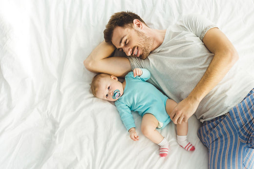 a father and a baby lying in white bamboo sheet