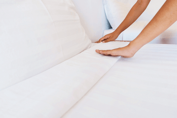 a person making her bed with white sheets