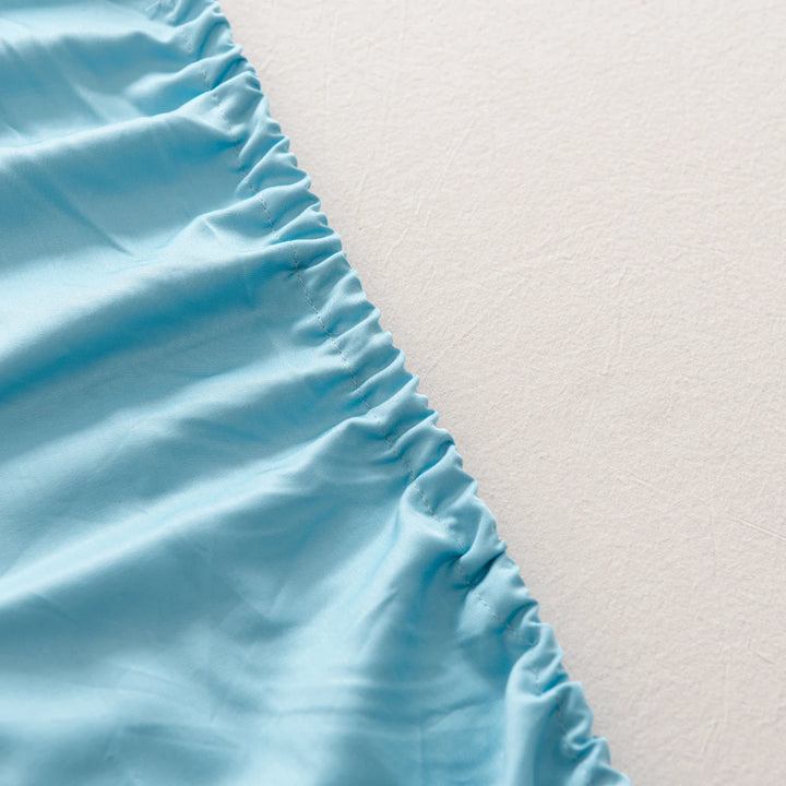 A close-up view of a ruffled edge of an Aqua Blue Linenly bamboo fitted sheet on a textured white background, showcasing the cooling effect of sustainably sourced bamboo fitted sheets.
