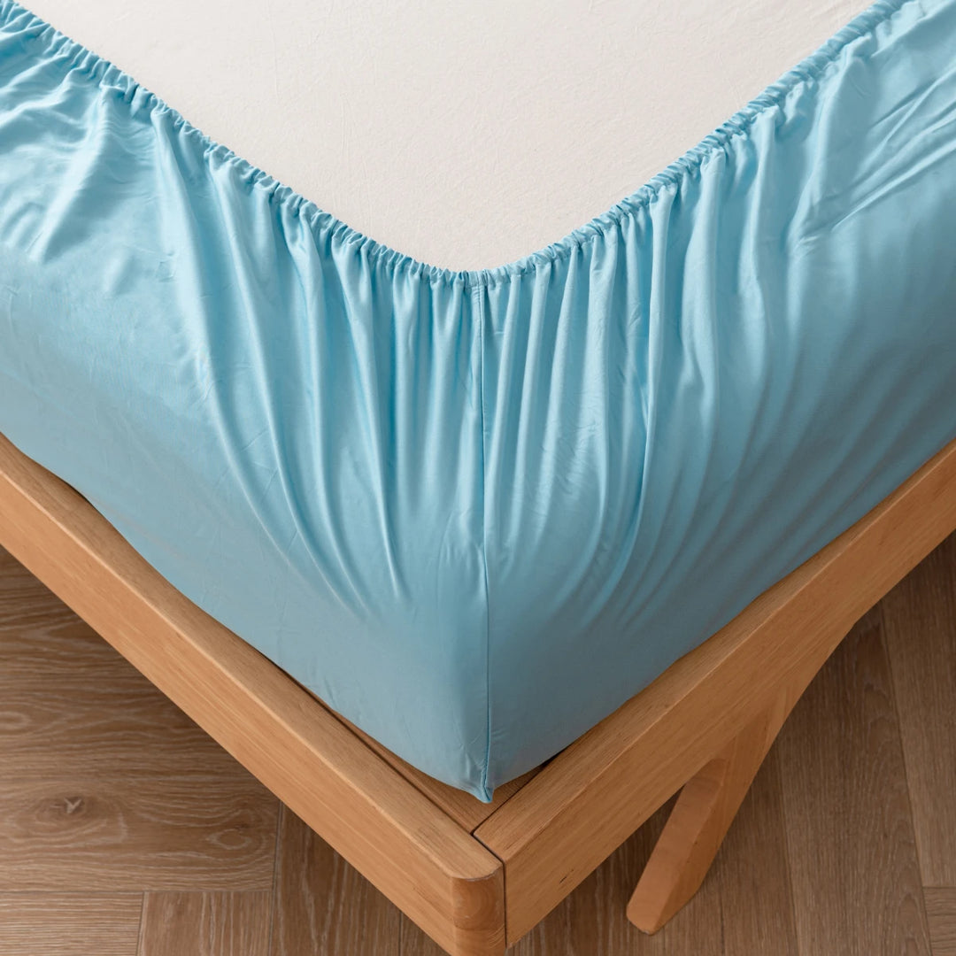 A neatly fitted, Linenly aqua blue bamboo fitted sheet on a wooden bed frame, showcasing a tidy corner of a bedroom.