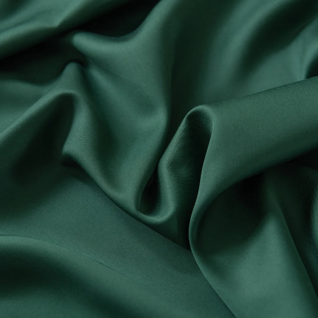 A close-up of Linenly's Bamboo Fitted Sheet Set - Evergreen reveals smooth, wavy emerald green fabric with gentle folds and a soft sheen, embodying the elegant texture of luxury bedding.