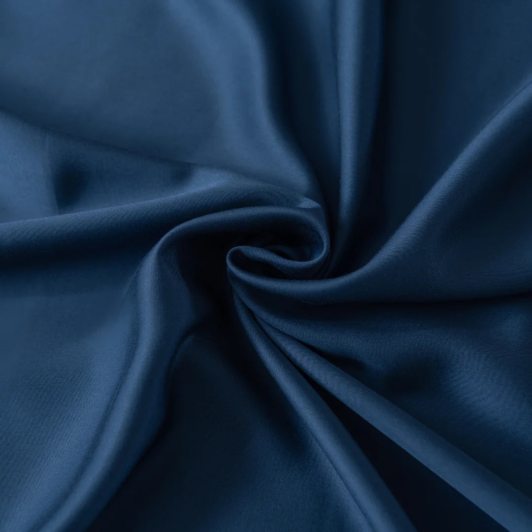 The Bamboo Fitted Sheet Set in Midnight by Linenly offers deep blue satin-like elegance with smooth, flowing folds that create a circular swirl design. Its glossy texture and gentle light reflections enhance its sheen, mirroring luxury bedding.