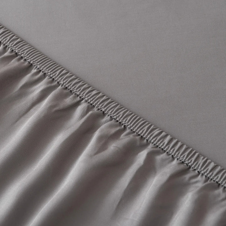 Linenly's Bamboo Fitted Sheet in Stone Grey is made of two different fabrics joined by a seam with overlock stitching, showcasing a contrast in luxuriously soft texture and sheen.