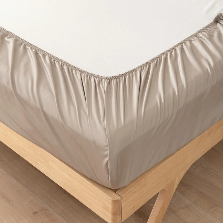 A Linenly Taupe Bamboo Fitted Sheet on a wooden bed frame, with a floor of laminated parquet.
