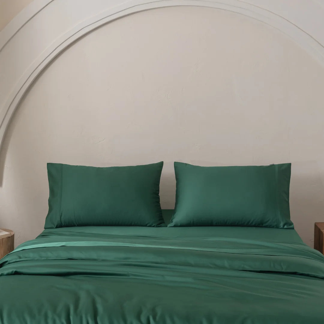 A neatly made bed features Linenly's Bamboo Quilt Cover Set in Evergreen, crafted from premium bamboo materials, with two matching pillows. It sits against a light cream wall, enhanced by an arched design above the bed for a decorative touch to the minimalist setting.