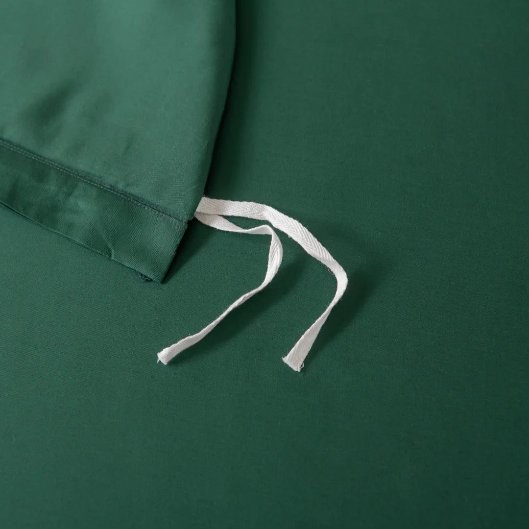 Flat-lay image of a dark green fabric drawstring bag on matching surface, made from premium bamboo materials. The white drawstrings contrast with the deep green background, echoing the essence of Linenly’s Bamboo Quilt Cover - Evergreen.