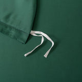 A close-up of Linenly's Bamboo Quilt Cover Set in Evergreen shows its silky texture with a drawstring edge on a flat surface. Two white strings tied against the solid green background evoke a restful sleep experience.