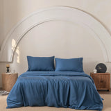 Centered in the room with beige walls and semicircular decor, a bed features two pillows with blue sheets, enveloped in Linenly's Bamboo Quilt Cover Set in Midnight. Wooden nightstands flanking the bed hold decorative items including a candle and clock.