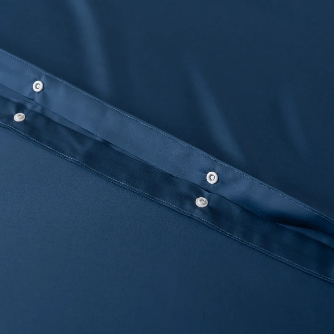 Close-up of dark blue Bamboo Quilt Cover - Midnight by Linenly, featuring a row of evenly spaced metal snap buttons along the seam. The unwrinkled fabric evokes a luxurious silky texture with an elegant touch.