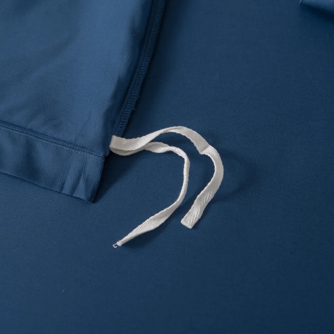 A close-up of Linenly's Bamboo Quilt Cover Set - Midnight shows a dark blue bamboo fabric bed sheet with a white tie string on top, loosely arranged across the sateen weave to highlight the quilt cover's texture and smoothness.