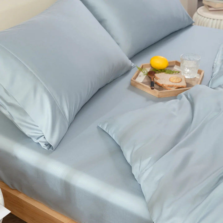 A cozy bedroom scene with an inviting bed made with a Linenly Bamboo Quilt Cover in Pale Blue, accompanied by soft pillows, a wooden tray holding a refreshing lemon, a glass of water, and a knife on a cutting board.