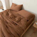 A neatly made bed features the Linenly Bamboo Quilt Cover Set in Terracotta, complemented by brown sheets and pillowcases on a wooden frame in a minimalist room with neutral walls, eco-friendly bedding, and a small side table.
