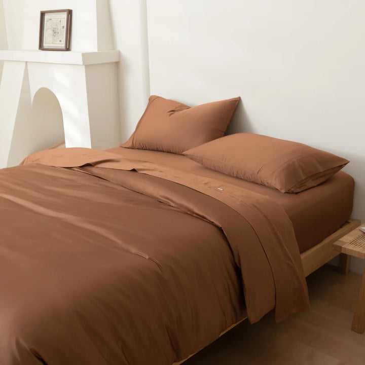 A neatly made bed with warm-toned brown, environmentally friendly Linenly bamboo quilt cover in a minimalist bedroom setting.