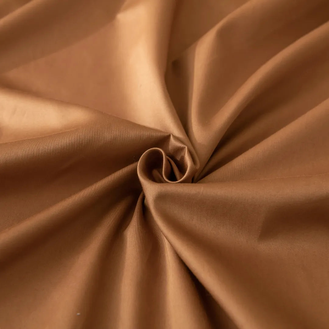 Close-up of the Linenly Luxe Cotton Sateen Fitted Sheet in Terracotta, showcasing its smooth, light brown long-staple cotton with a soft sheen, gathered at the center to reveal gentle folds and a spiral pattern.