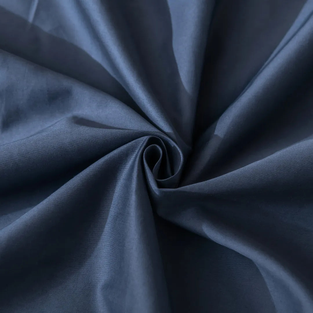 A close-up of smooth dark blue fabric with spiral folds highlights the soft, slightly shiny texture of Linenly’s Luxe Cotton Sateen Pillowcase Set - Midnight, capturing its premium elegance.