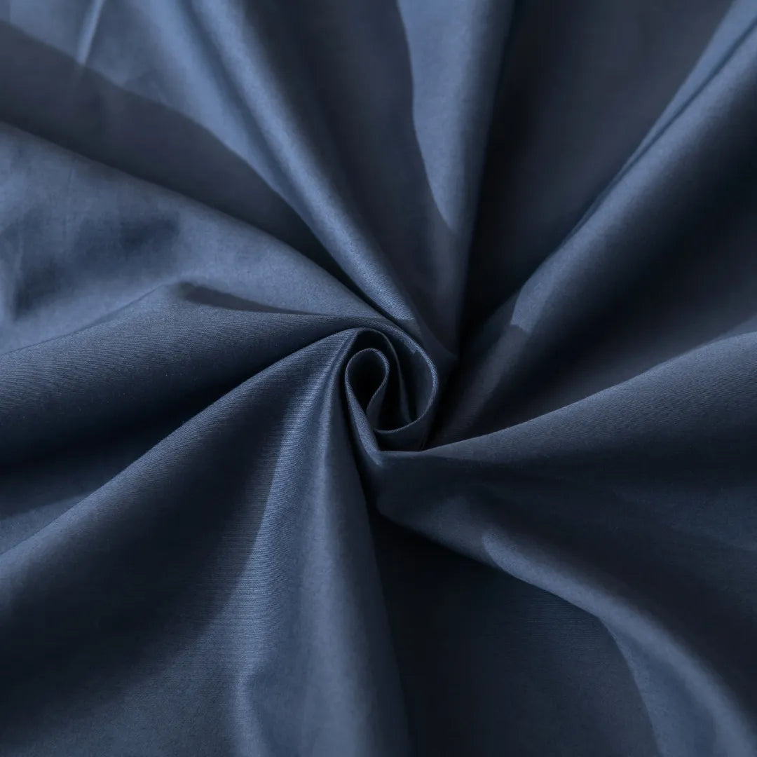 A close-up of Linenly’s Luxe Cotton Sateen Quilt Cover in Midnight, twisted into a spiral, reveals soft folds and gentle shadows across its smooth surface.