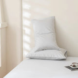 Two white pillows rest on a neatly made bed featuring the Luxe Cotton Sateen Sheet Set in Silver by Linenly. A cup and saucer on a tray complete the tranquil setting as soft light filters through the window.