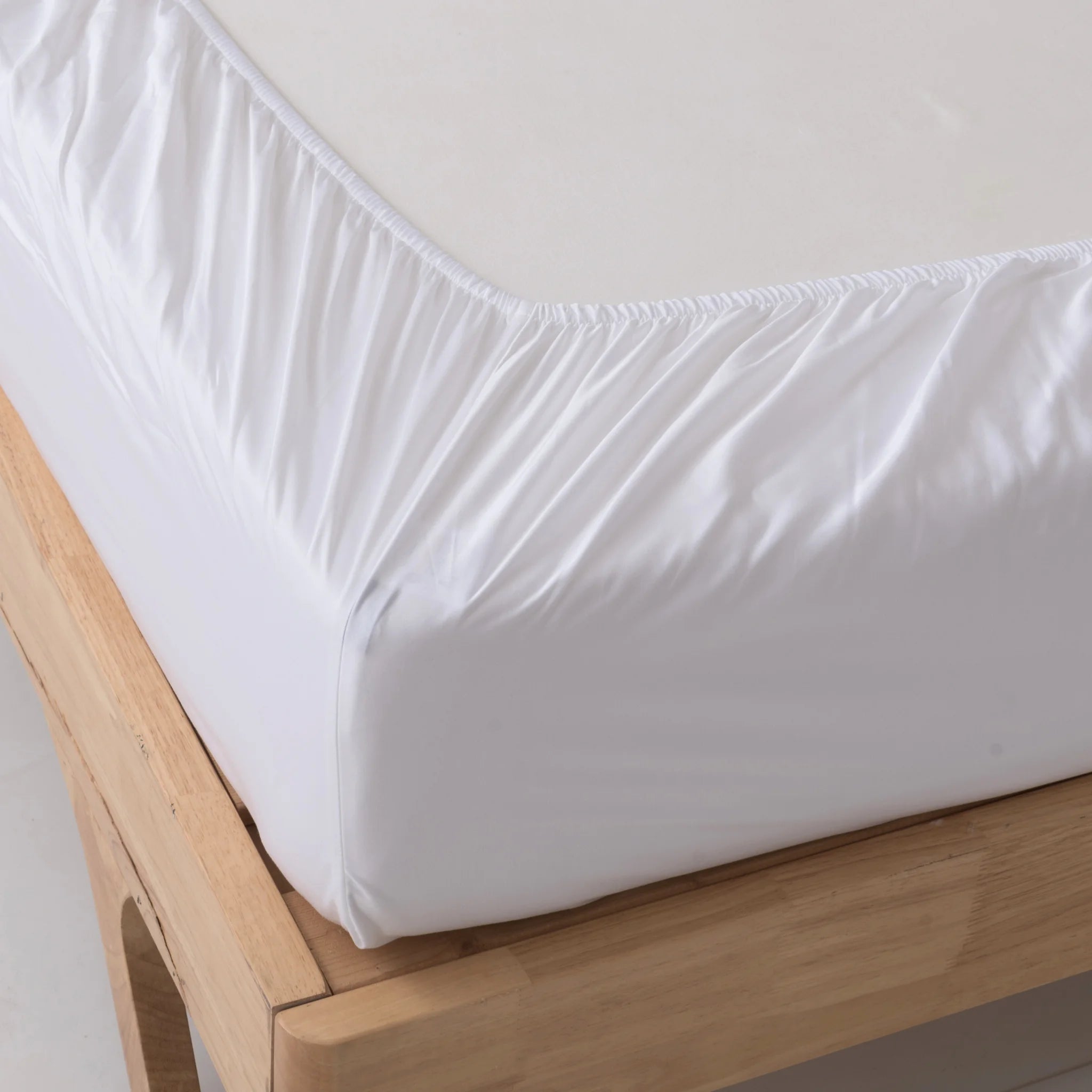 A close-up of the Linenly Bamboo Fitted Sheet - White, snugly covering a mattress on a light wooden bed frame. The sheet appears smooth and luxurious, while the frame features clean, sleek edges.